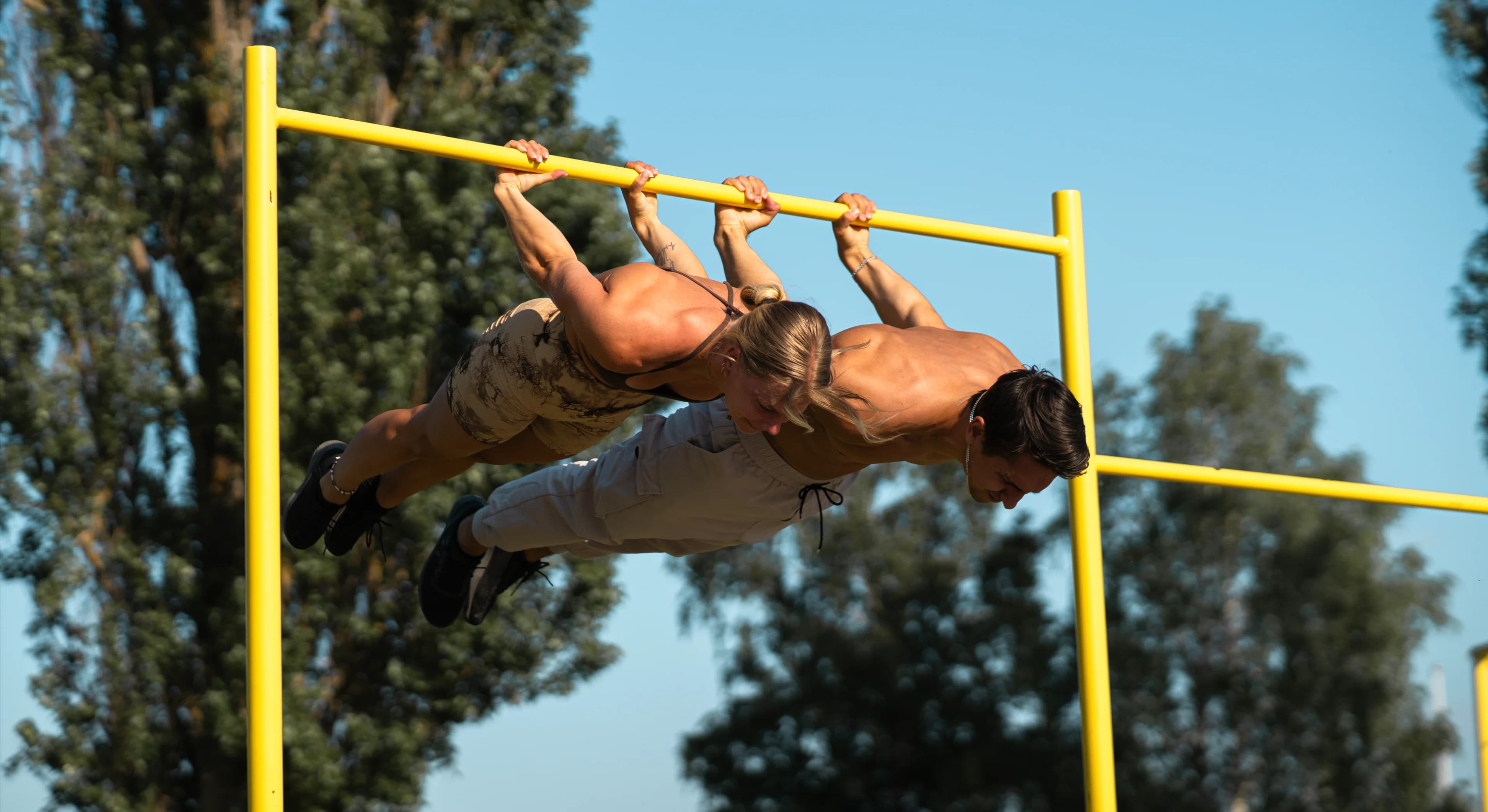 Daniel Flefil and Malin Malle Jansson performing back levers side by side on a calisthenics bar outdoors in Stockholm.