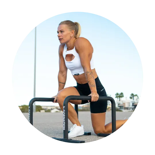 Kvinna som utför en calisthenics-övning på paralletter i vit träningstopp och svarta shorts.