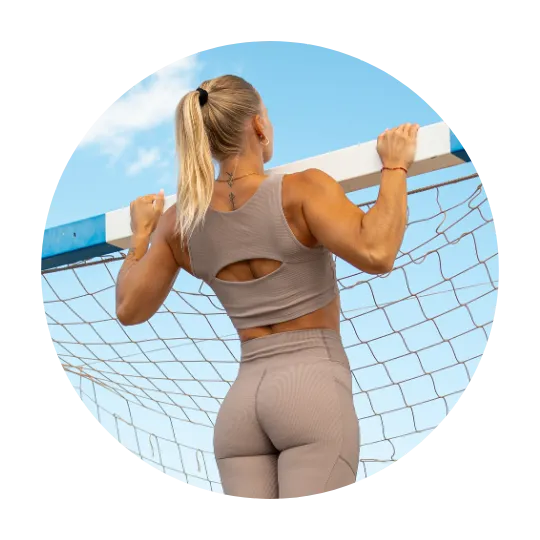Kvinna som utför pull-up på en horisontell stång i beige träningskläder med klar blå himmel i bakgrunden.