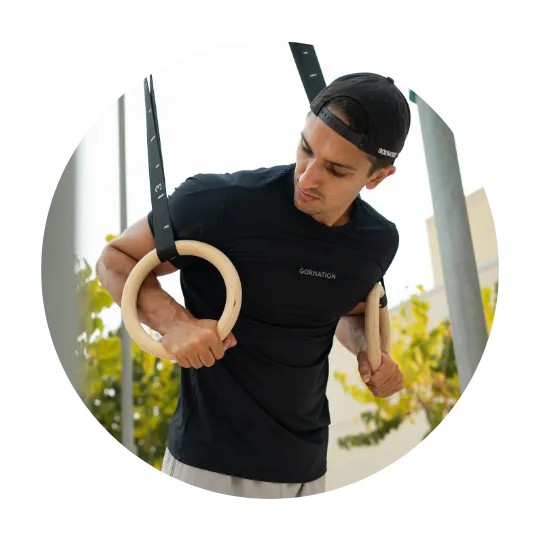 Man som utför ring-dip utomhus i svart t-shirt och grå shorts.